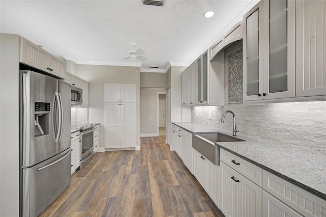 kitchen featuring appliances with stainless steel finishes, ceiling fan, crown molding, dark wood-type flooring, and sink