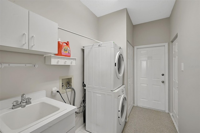 washroom with cabinets, stacked washer / dryer, and sink