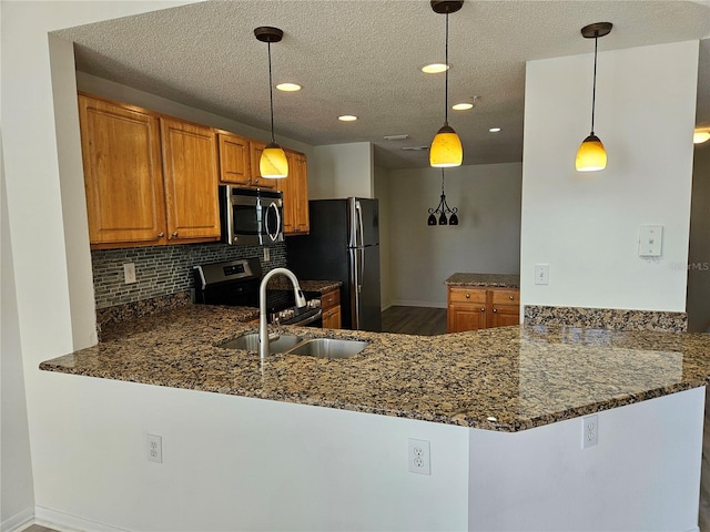 kitchen with hanging light fixtures, sink, dark stone countertops, appliances with stainless steel finishes, and kitchen peninsula