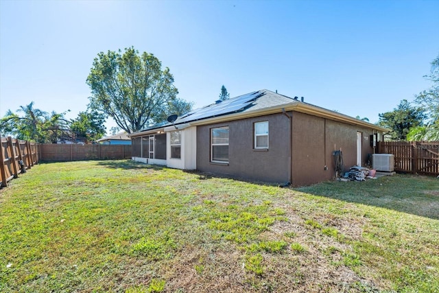 rear view of property with a lawn, solar panels, central AC unit, and a sunroom