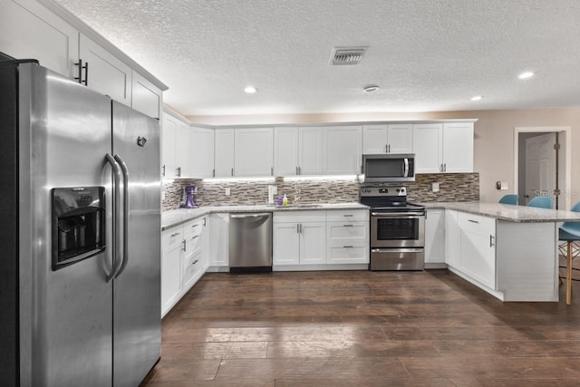 kitchen featuring kitchen peninsula, appliances with stainless steel finishes, light stone counters, white cabinets, and dark hardwood / wood-style floors