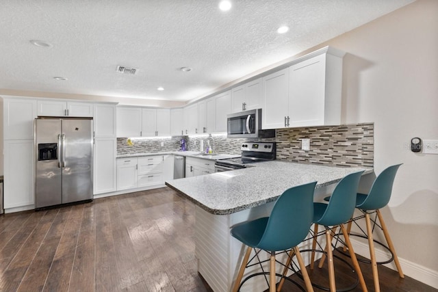 kitchen with white cabinets, dark hardwood / wood-style flooring, stainless steel appliances, and kitchen peninsula