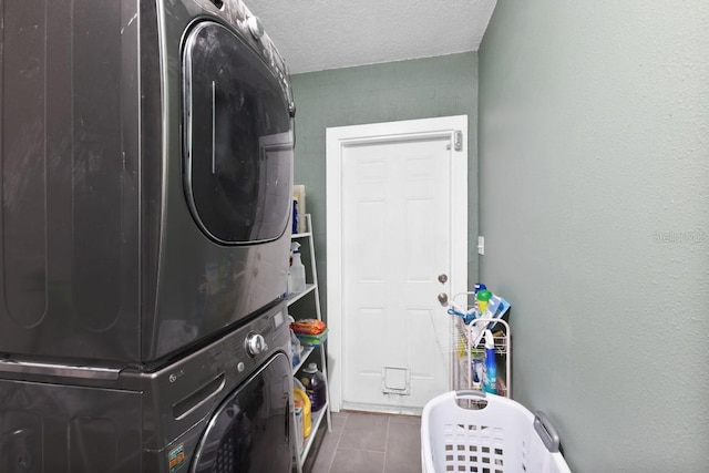 washroom with a textured ceiling, dark tile patterned floors, and stacked washer / dryer