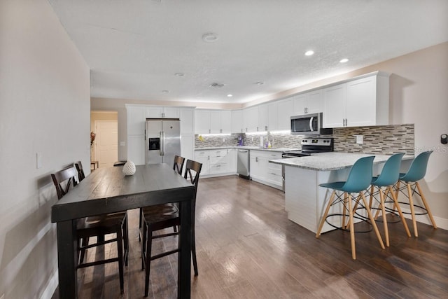 dining room featuring a breakfast bar area, light stone countertops, white cabinets, dark hardwood / wood-style floors, and kitchen peninsula