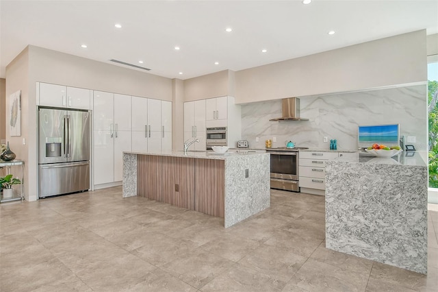 kitchen featuring white cabinetry, a center island with sink, wall chimney exhaust hood, and stainless steel appliances