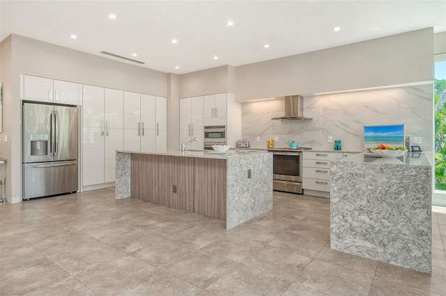 kitchen featuring appliances with stainless steel finishes, a center island with sink, white cabinetry, and wall chimney exhaust hood