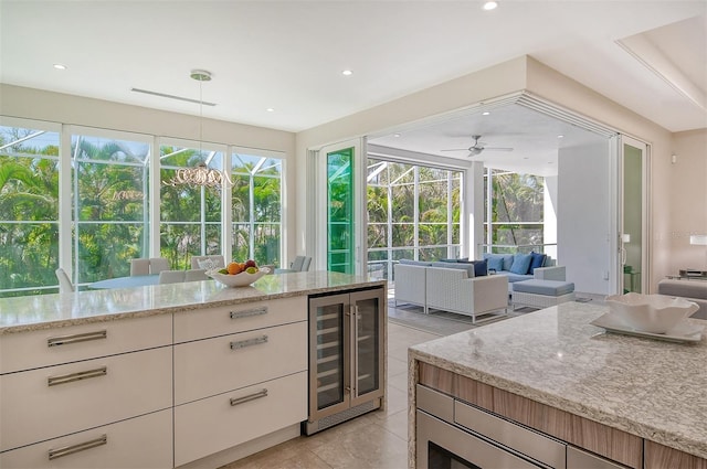 kitchen with pendant lighting, a healthy amount of sunlight, light stone counters, and beverage cooler