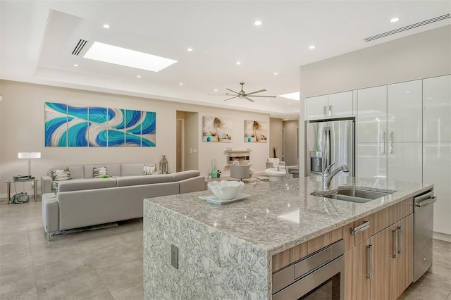 kitchen with light stone countertops, appliances with stainless steel finishes, sink, white cabinetry, and an island with sink