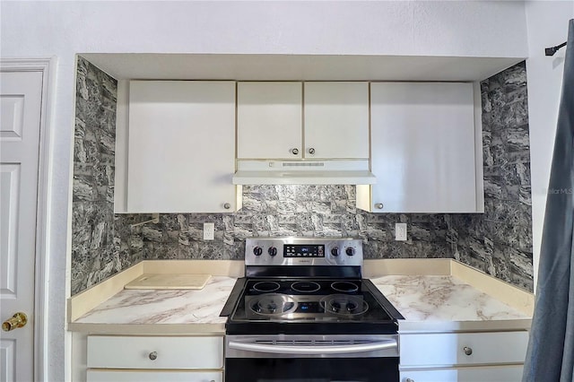 kitchen with stainless steel electric stove, backsplash, and white cabinetry