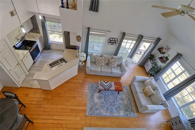 living room with a high ceiling, light hardwood / wood-style floors, ceiling fan, and sink