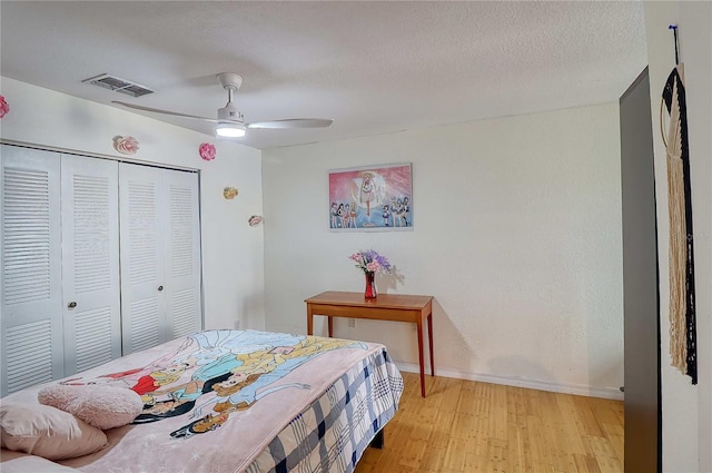 bedroom featuring a textured ceiling, a closet, light hardwood / wood-style flooring, and ceiling fan