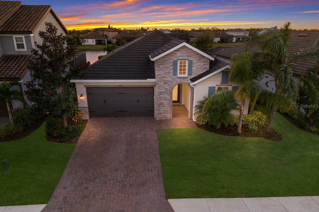 traditional-style home with stone siding, decorative driveway, a front yard, and a tiled roof