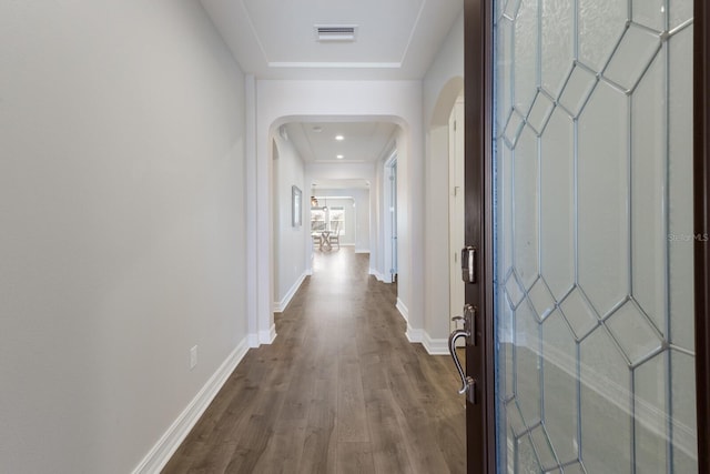 hall featuring baseboards, visible vents, arched walkways, and wood finished floors