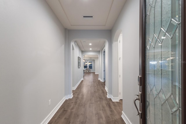 corridor featuring baseboards, visible vents, arched walkways, and wood finished floors