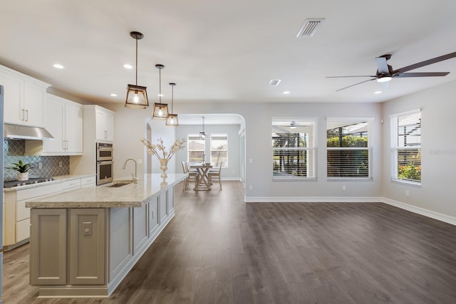 kitchen with a center island with sink, appliances with stainless steel finishes, decorative light fixtures, under cabinet range hood, and white cabinetry