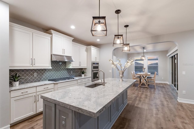 kitchen with arched walkways, hanging light fixtures, white cabinetry, a sink, and under cabinet range hood