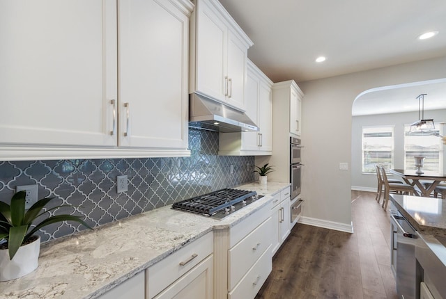 kitchen featuring arched walkways, under cabinet range hood, stainless steel appliances, white cabinets, and decorative light fixtures