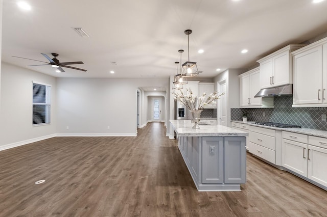 kitchen with a kitchen island with sink, under cabinet range hood, visible vents, white cabinetry, and open floor plan