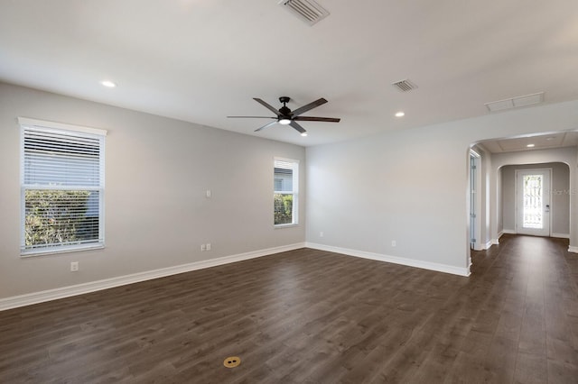 empty room featuring arched walkways, a wealth of natural light, dark wood finished floors, and visible vents