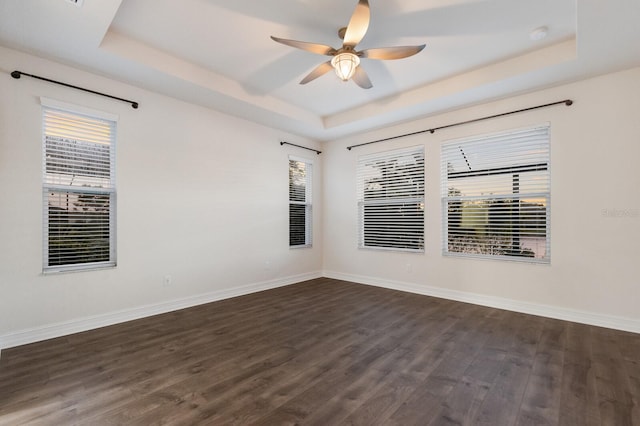 empty room featuring dark wood-style floors, a raised ceiling, ceiling fan, and baseboards