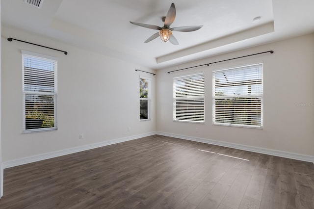 spare room with a tray ceiling, dark wood-style flooring, a ceiling fan, and baseboards