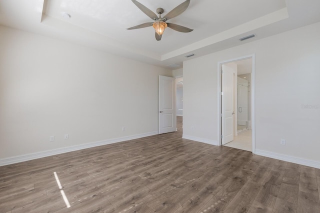 unfurnished bedroom with a tray ceiling, wood finished floors, visible vents, and baseboards