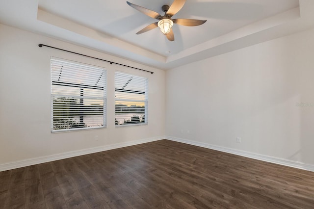 unfurnished room featuring a ceiling fan, a raised ceiling, dark wood finished floors, and baseboards