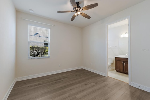 unfurnished bedroom with light wood-style floors, ceiling fan, baseboards, and ensuite bathroom