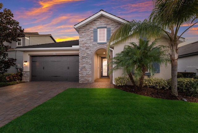 view of front facade with a garage, stone siding, a yard, and decorative driveway