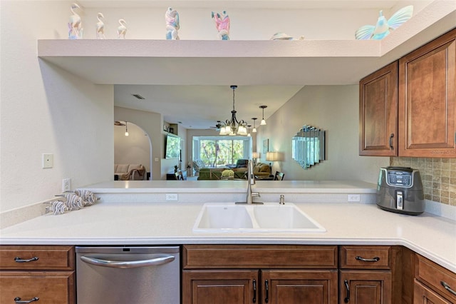 kitchen featuring tasteful backsplash, stainless steel dishwasher, sink, pendant lighting, and a notable chandelier