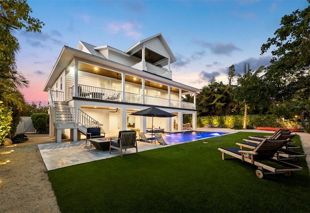 back house at dusk with a yard, a patio area, ceiling fan, and a balcony