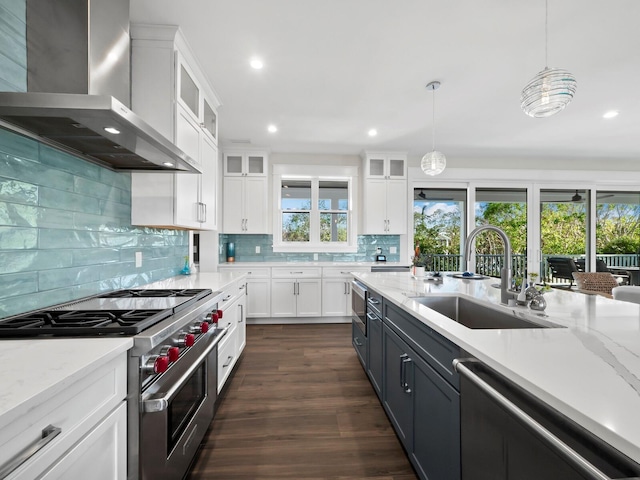 kitchen with white cabinetry, sink, wall chimney range hood, pendant lighting, and appliances with stainless steel finishes