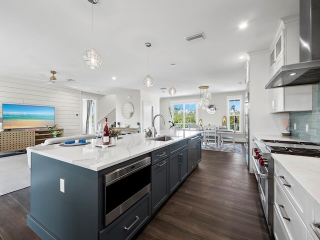 kitchen featuring pendant lighting, a center island with sink, sink, wall chimney exhaust hood, and stainless steel range