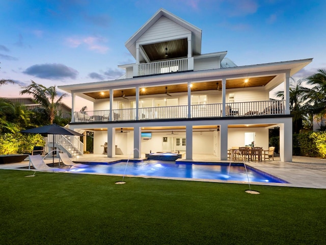 back house at dusk featuring an outdoor bar, pool water feature, ceiling fan, a balcony, and a patio area