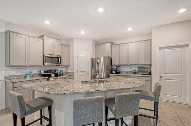 kitchen with a kitchen bar, gray cabinetry, an island with sink, and appliances with stainless steel finishes