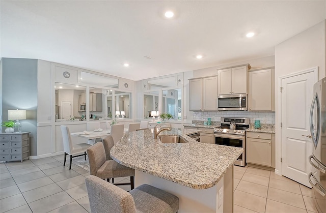 kitchen with a kitchen bar, light stone countertops, stainless steel appliances, a kitchen island with sink, and sink