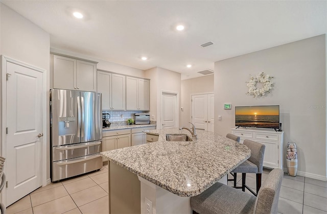 kitchen featuring stainless steel fridge with ice dispenser, a center island with sink, light stone counters, and sink