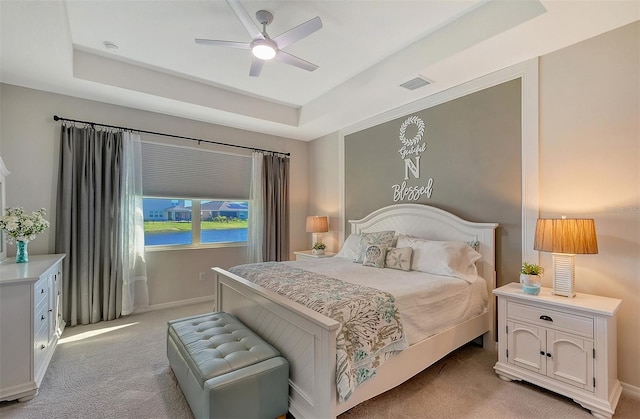 carpeted bedroom featuring a raised ceiling and ceiling fan