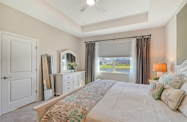 carpeted bedroom featuring a tray ceiling, multiple windows, and ceiling fan