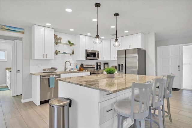 kitchen featuring stainless steel appliances, a kitchen island, sink, white cabinetry, and hanging light fixtures