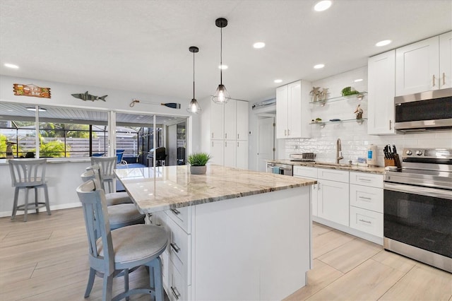 kitchen with a center island, stainless steel appliances, light stone counters, decorative light fixtures, and white cabinets