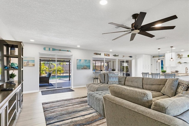 living room with ceiling fan, a textured ceiling, and light wood-type flooring