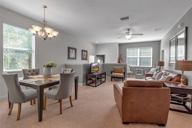 dining room with light colored carpet, a healthy amount of sunlight, and ceiling fan with notable chandelier