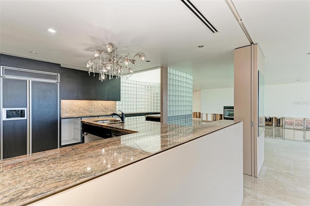 kitchen with light stone countertops, sink, decorative light fixtures, and paneled refrigerator