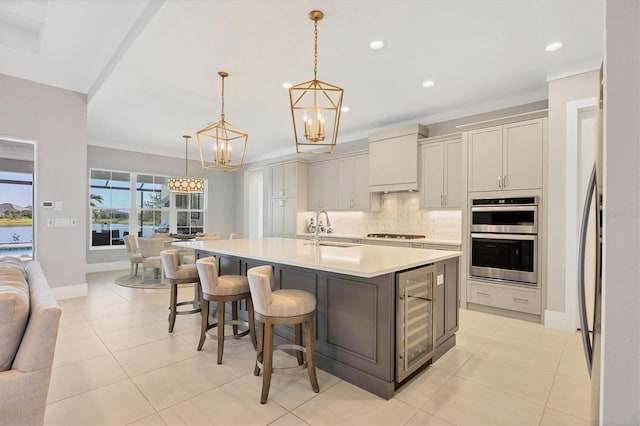 kitchen with sink, wine cooler, pendant lighting, a center island with sink, and custom exhaust hood