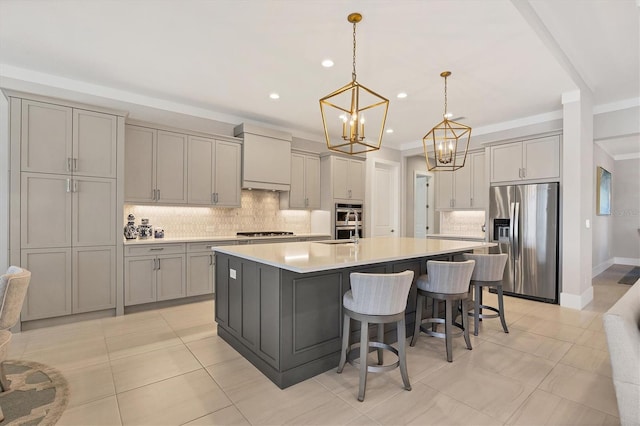 kitchen featuring appliances with stainless steel finishes, a large island with sink, gray cabinets, hanging light fixtures, and a breakfast bar area