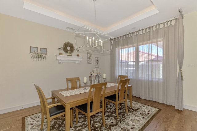 dining space with a notable chandelier, a raised ceiling, and wood-type flooring