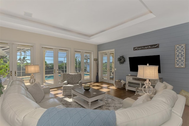 living room with hardwood / wood-style flooring, wooden walls, a tray ceiling, and french doors