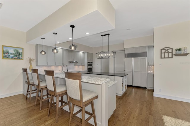 kitchen with gray cabinetry, decorative backsplash, light wood-type flooring, and hanging light fixtures