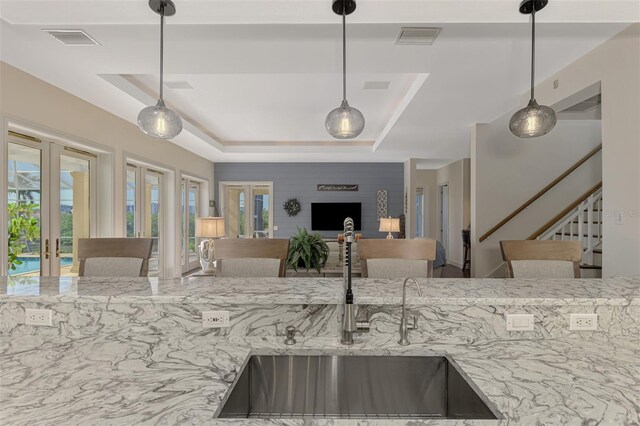 kitchen featuring light stone countertops, french doors, sink, a raised ceiling, and pendant lighting